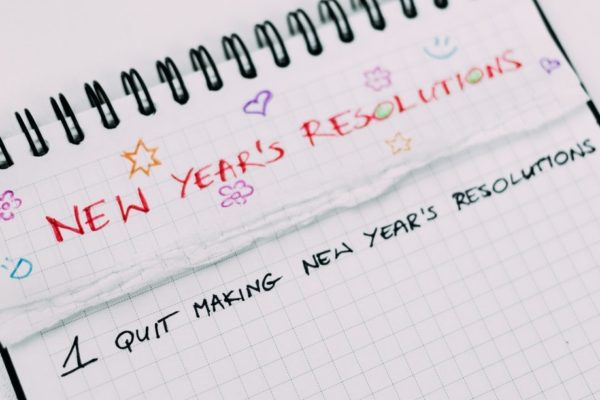 A notebook with 'New Years' Resolutions" written at the top, and the first line being "Stop making New Years' Resolutions"