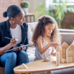 A mom watches her daughter build with blocks.