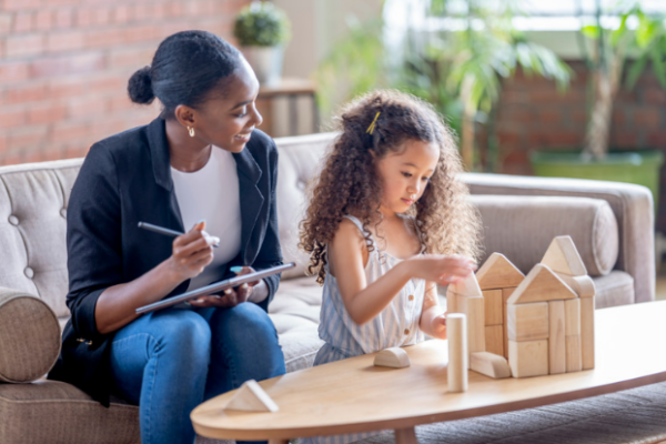 A mom watches her daughter build with blocks.