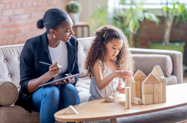 A mom watches her daughter build with blocks.