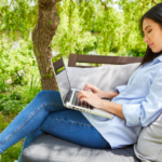 A woman sitting outside working on her laptop.