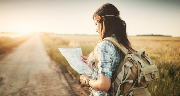 A female hiker studies a map while standing next to a road.