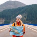 A young woman studies a road map while standing on a road.