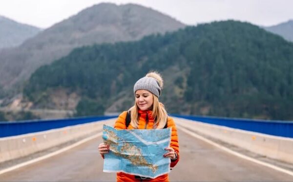 A young woman studies a road map while standing on a road.