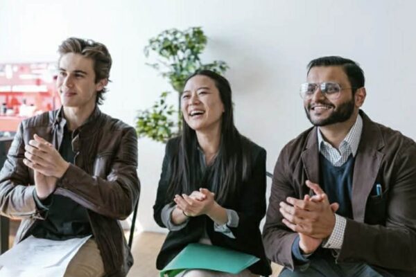 Three agents, two male, one female, applaud a pitch.