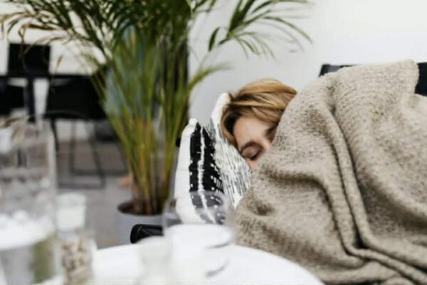 A woman sleeps on a sofa, cocooned in a blanket