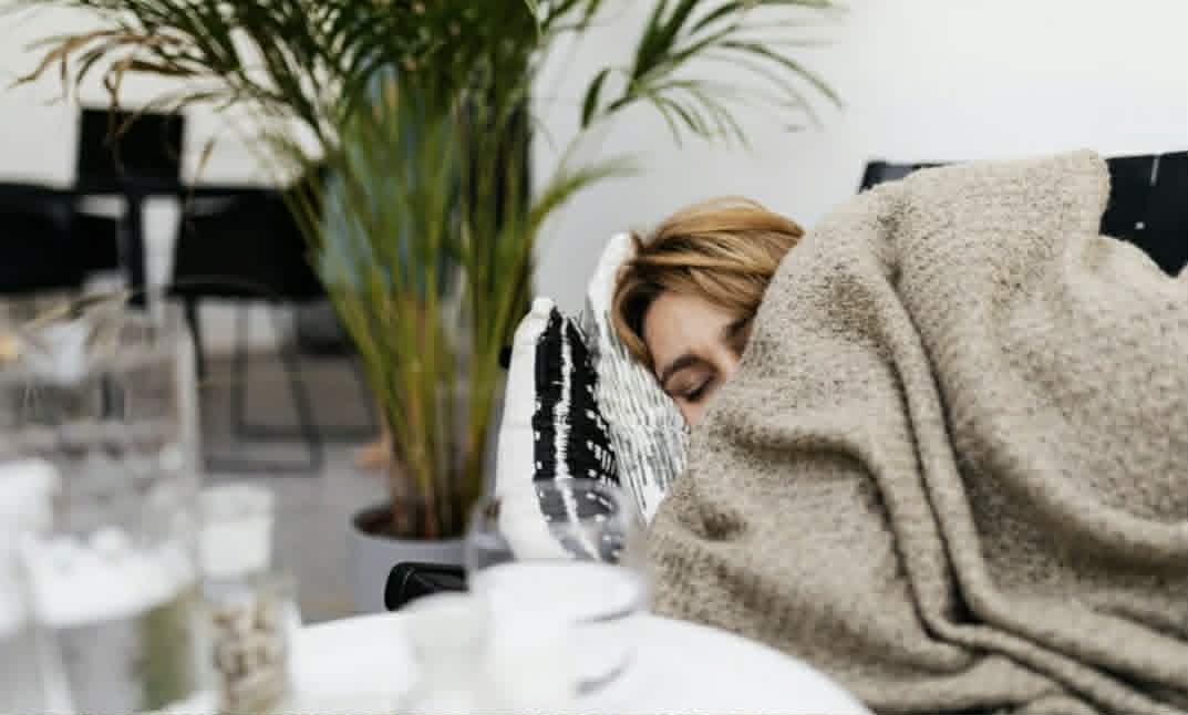 A woman sleeps on a sofa, cocooned in a blanket