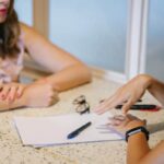 Two women discuss a written manuscript.