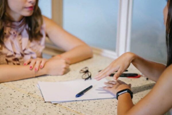 Two women discuss a written manuscript.