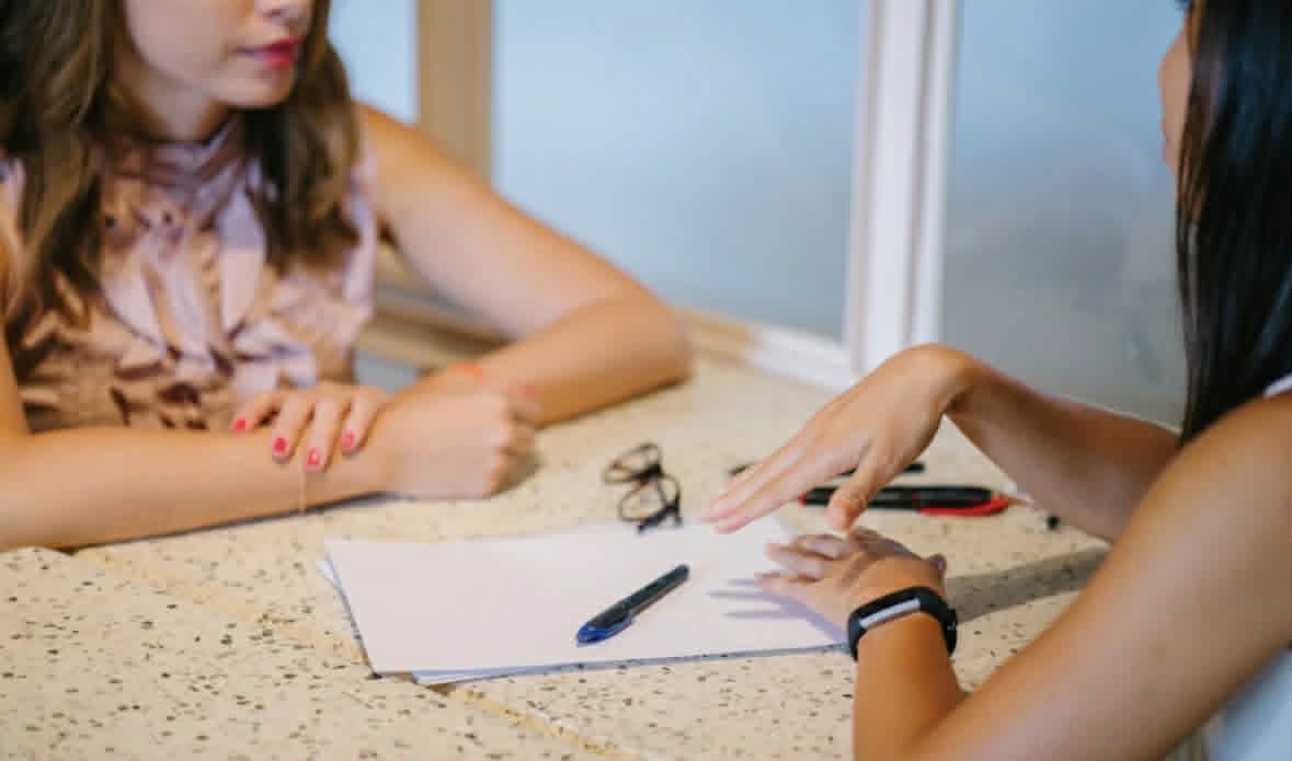 Two women discuss a written manuscript.