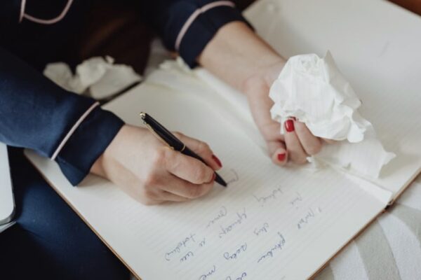 A closeup of a writer's hands, one holding a pen and the other holding a tissue.