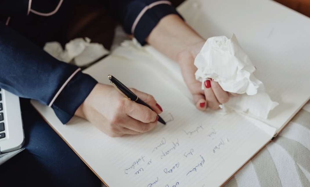 A closeup of a writer's hands, one holding a pen and the other holding a tissue.