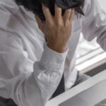 A man sitting with a desk with his head in his hands.