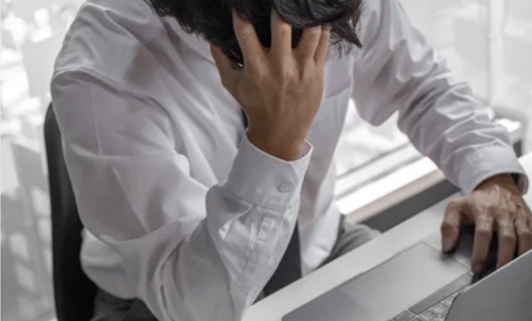 A man sitting with a desk with his head in his hands.