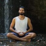 A man sits on the forest floor in a meditative pose.