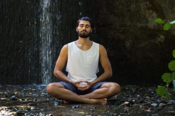 A man sits on the forest floor in a meditative pose.