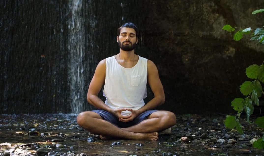 A man sits on the forest floor in a meditative pose.